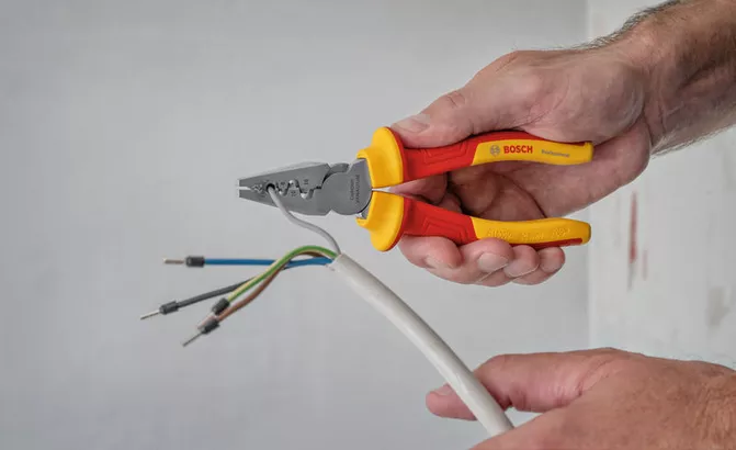 Orang melepaskan isolasi dari kabel listrik menggunakan tang berisolasi.