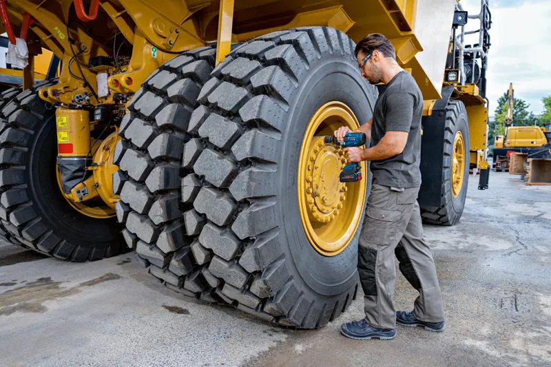 Seseorang yang mengenakan peralatan keselamatan menggunakan kunci pas benturan pada ban kendaraan konstruksi berukuran besar.