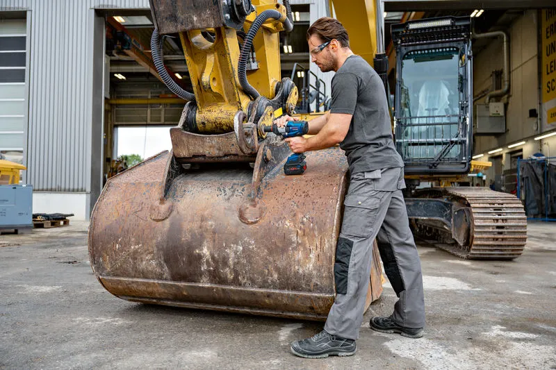 Seseorang yang mengenakan peralatan keselamatan menggunakan kunci pas benturan pada mesin konstruksi berat.