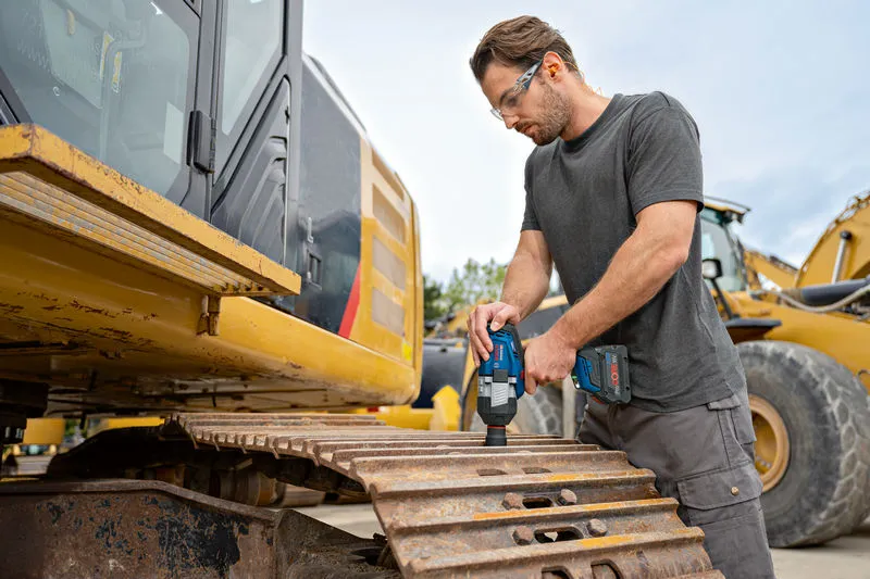 Seseorang yang mengenakan perlengkapan keselamatan menggunakan kunci pas benturan tanpa kabel di lintasan ekskavator.