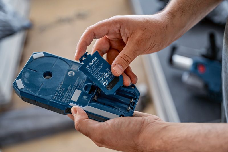 Seseorang memasukkan paket baterai ke dalam rumah perkakas listrik berwarna biru.