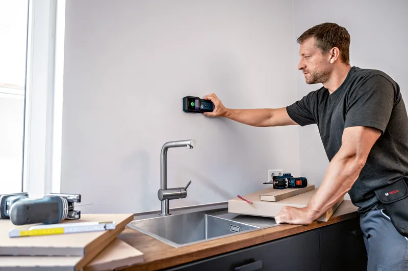 GMS 120-27 Seseorang memindai dinding dapur di atas wastafel dengan alat detektor digital.