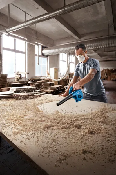 Blower Bosch GBL 650 membersihkan serbuk gergaji dari meja kerja.