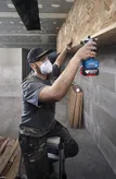 Seseorang yang mengenakan peralatan keselamatan menggunakan router di rak kayu.