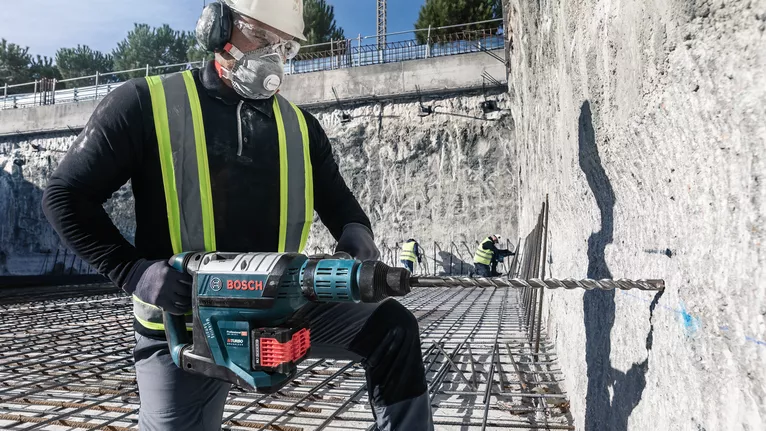 Mata Bor Hammer PRO SDS max-4, 12 x 200 x 340 mm Pekerja yang mengenakan peralatan keselamatan menggunakan bor palu putar pada dinding beton di lokasi konstruksi.