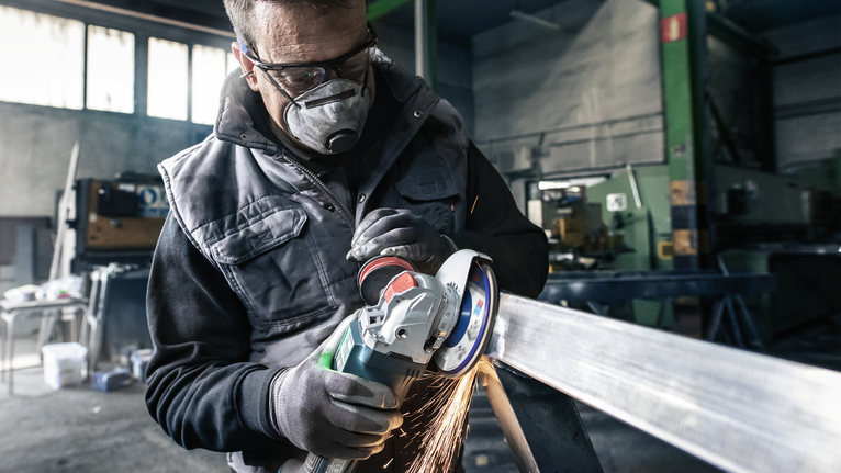 Orang yang mengenakan peralatan keselamatan menggiling balok logam, sehingga menimbulkan percikan api.