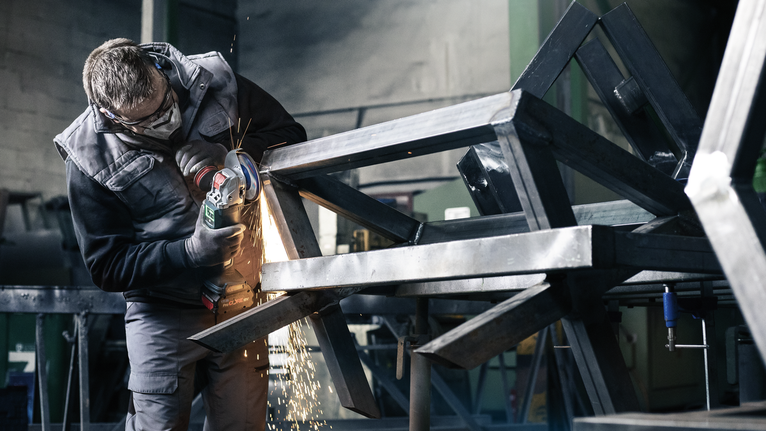 Seseorang yang mengenakan peralatan keselamatan menggesek rangka logam, sehingga menimbulkan percikan api.