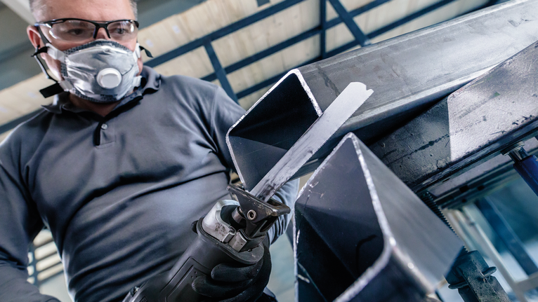 Orang yang mengenakan peralatan keselamatan menggunakan gergaji bolak-balik untuk memotong balok logam.