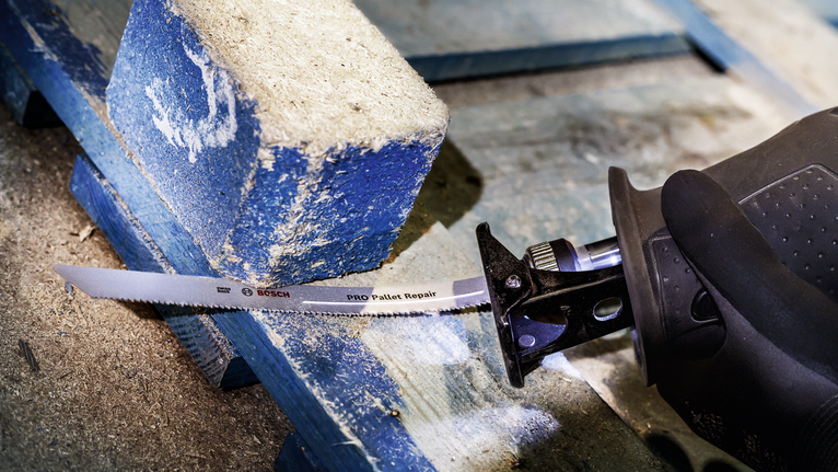 Orang yang mengenakan peralatan keselamatan memotong palet kayu dengan gergaji bolak-balik.