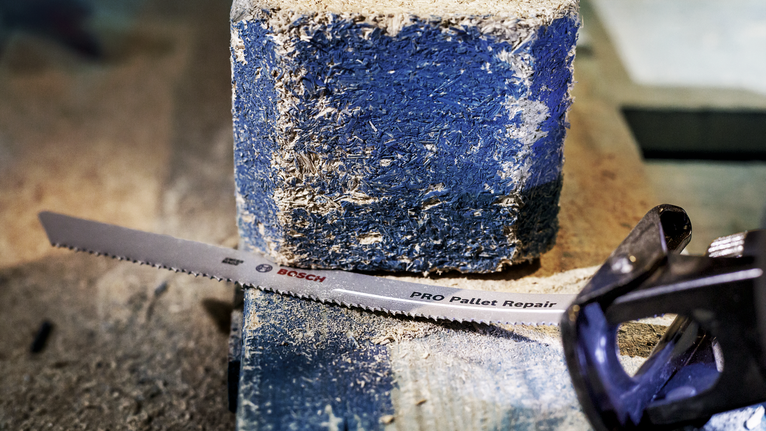 Mata gergaji bolak-balik diletakkan di atas blok palet kayu yang berdebu.