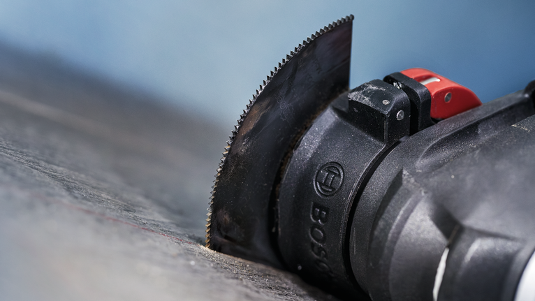 Alat multifungsi berosilasi dengan bilah lurus yang memotong permukaan gelap.