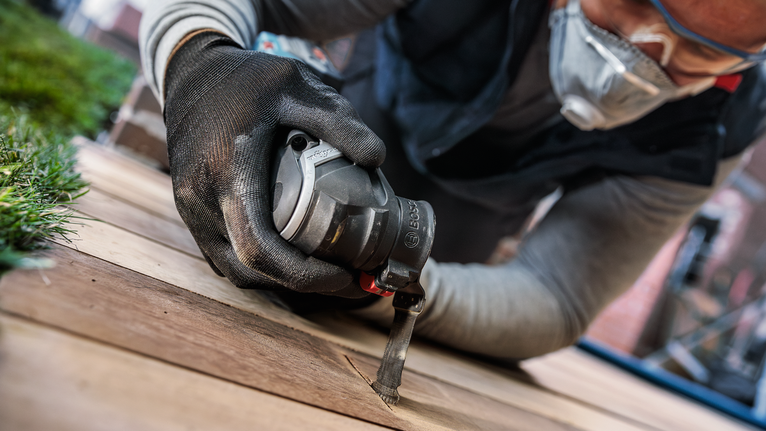 Orang yang mengenakan peralatan keselamatan menggunakan alat listrik untuk memotong papan kayu.