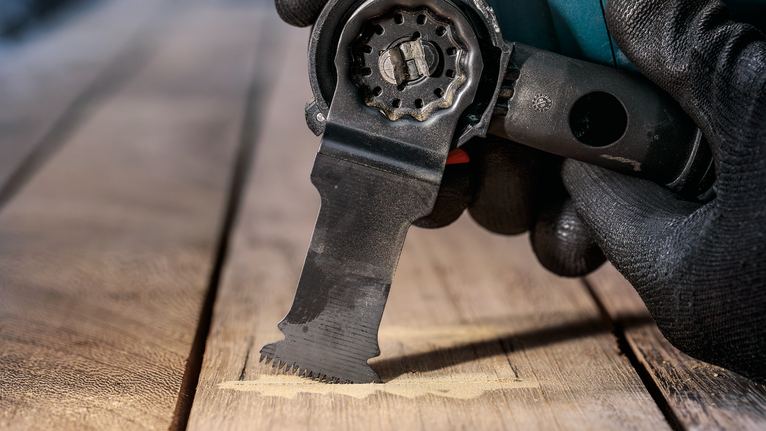 Orang yang mengenakan peralatan keselamatan menggunakan alat serbaguna untuk memotong kayu.