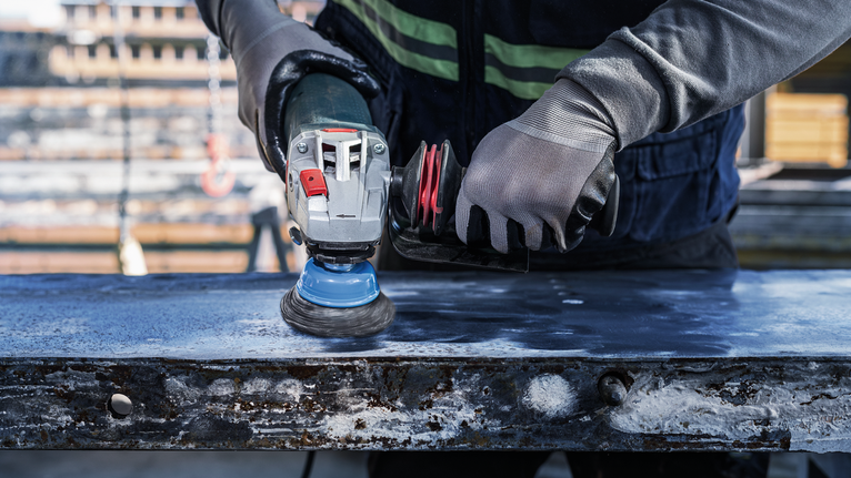 Orang yang mengenakan peralatan keselamatan memoles permukaan logam dengan perkakas listrik.