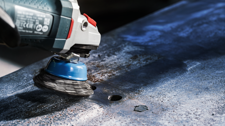 Penggiling sikat cangkir kawat menghilangkan karat dari lembaran logam.