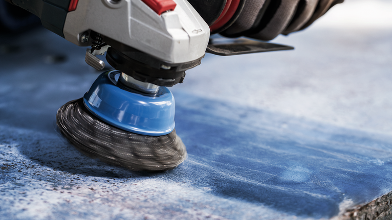 Orang yang mengenakan peralatan keselamatan menggiling permukaan batu biru dengan sikat kawat.