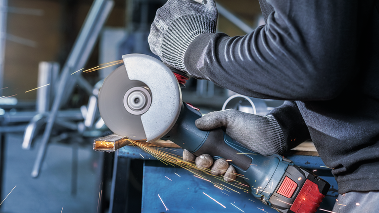 Orang yang mengenakan peralatan keselamatan menggiling logam, menghasilkan percikan api.