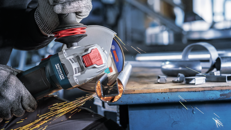 Seseorang yang mengenakan peralatan keselamatan menggiling pipa logam, sehingga menimbulkan percikan api.