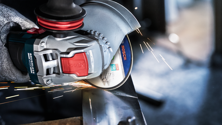 Seseorang yang mengenakan peralatan keselamatan menggiling logam, sehingga menghasilkan percikan terang.