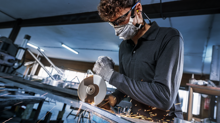 Orang yang mengenakan peralatan keselamatan memotong logam dengan penggiling sudut, percikan api beterbangan.