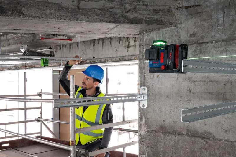 Seseorang yang mengenakan perlengkapan keselamatan menyelaraskan batang logam menggunakan alat perata laser.