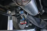 Seseorang yang mengenakan peralatan keselamatan mengencangkan baut pada kolong mobil dengan kunci pas benturan tanpa kabel.