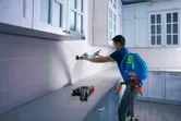Orang yang sedang menyelaraskan lemari dapur dengan alat perataan laser pada tripod.