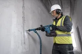 Seseorang yang mengenakan perlengkapan keselamatan menggunakan palu pembongkaran tanpa kabel untuk menghancurkan dinding beton.