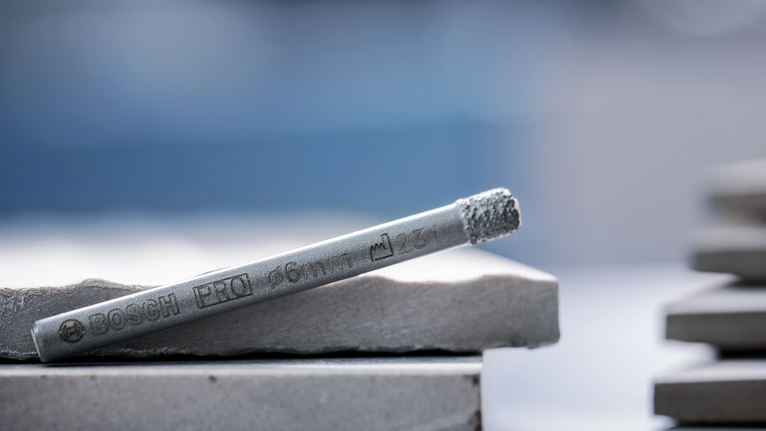 Mata bor logam diletakkan di atas tumpukan ubin batu.