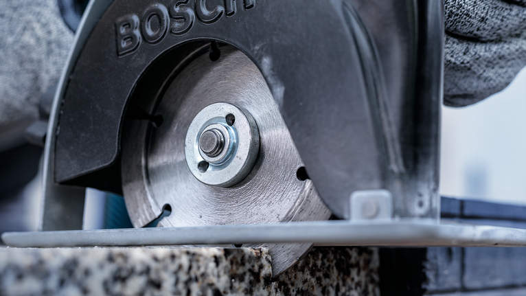 Orang yang mengenakan peralatan keselamatan memotong batu dengan gergaji bundar.