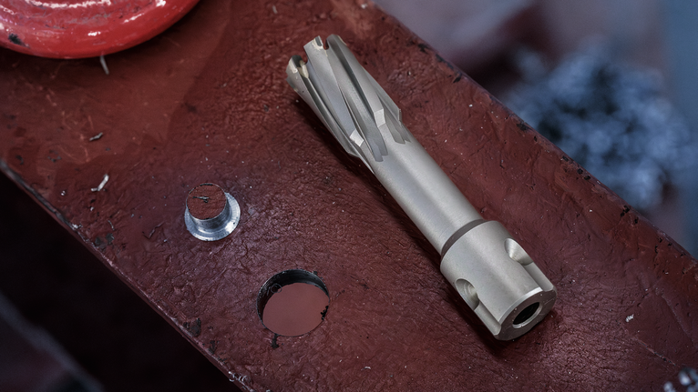 Pemotong melingkar dan lubang bor pada permukaan balok logam.