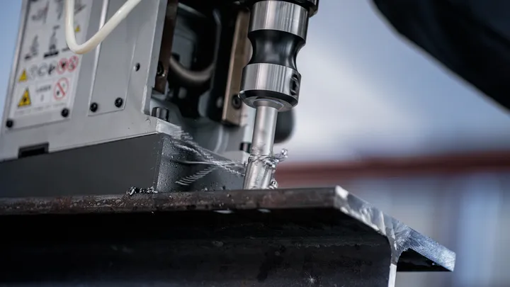 Bor inti memotong balok logam tebal dalam lingkungan industri.