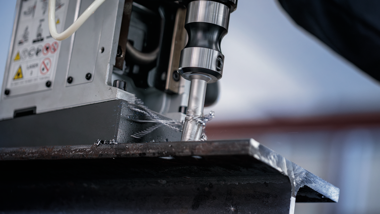 Bor inti memotong balok logam tebal dalam lingkungan industri.