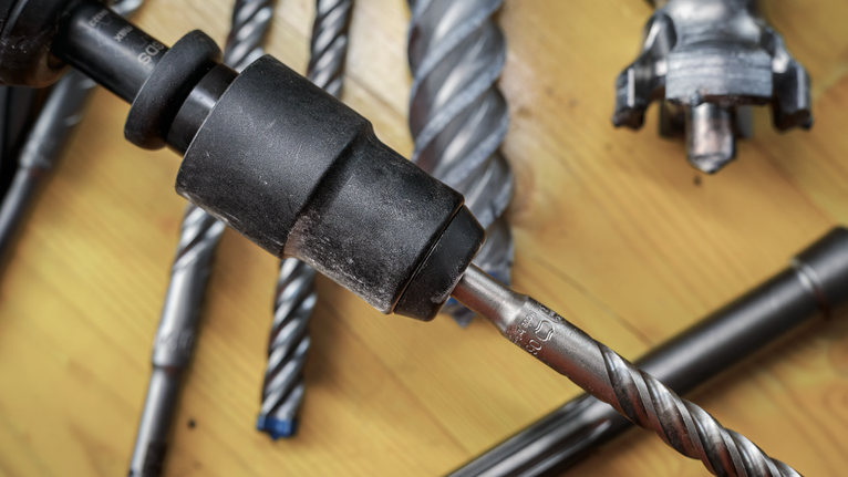 Tampilan dekat berbagai mata bor logam dan chuck bor pada permukaan kayu.