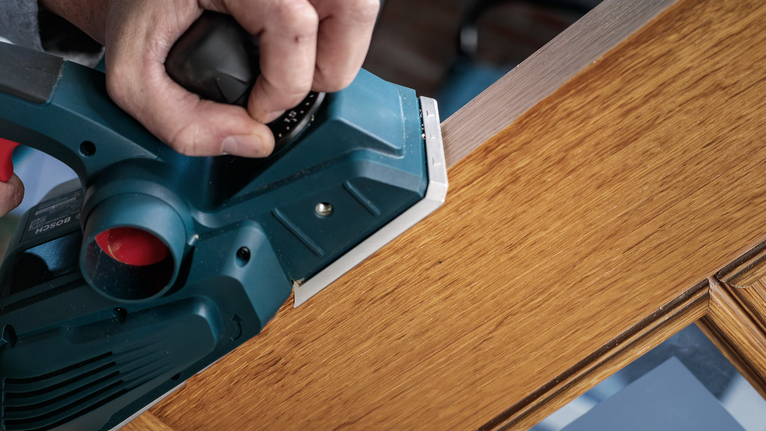 Alat serut listrik menghaluskan tepian pintu kayu.