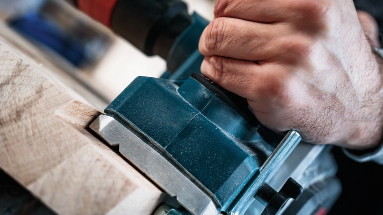 Orang menggunakan alat listrik untuk membentuk kayu.