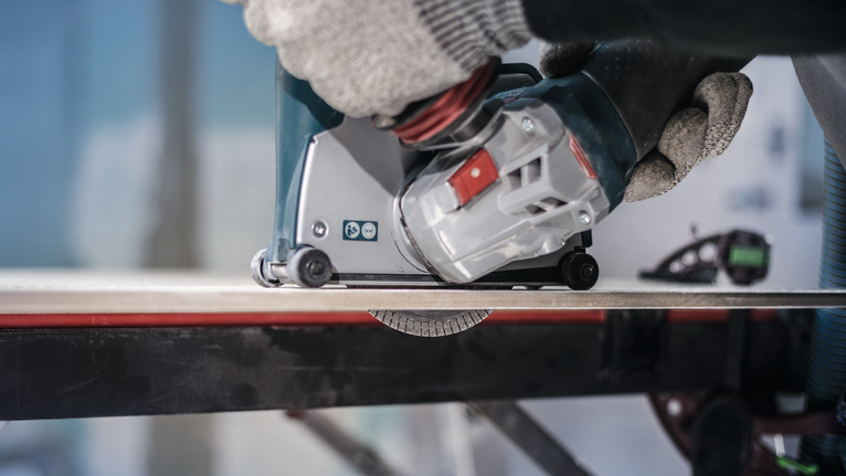 Orang yang mengenakan peralatan keselamatan mengoperasikan alat listrik untuk memotong ubin.