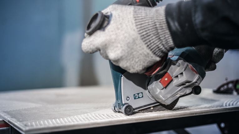 Orang yang mengenakan peralatan keselamatan menggunakan alat listrik untuk memotong ubin.