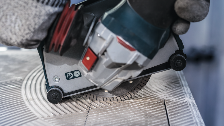 Orang yang mengenakan peralatan keselamatan menggunakan gergaji bundar untuk memotong ubin keramik.
