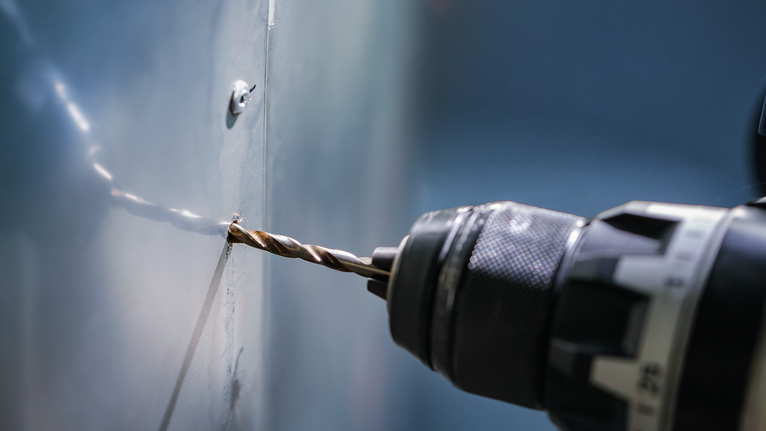 Bor listrik membuat lubang di panel logam.