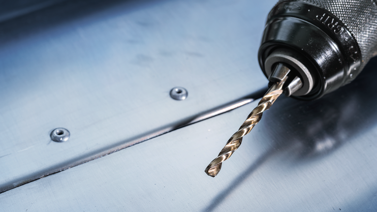 Gambar jarak dekat dari bor listrik dengan mata bor logam yang diletakkan pada permukaan baja.