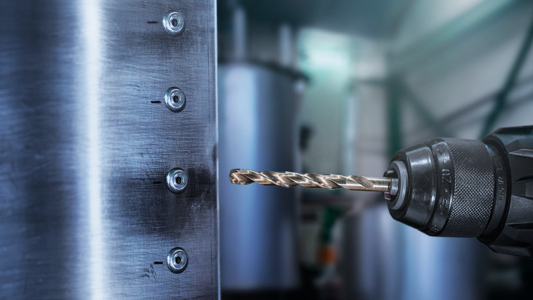 Bor listrik membuat lubang pada lembaran logam di bengkel industri.