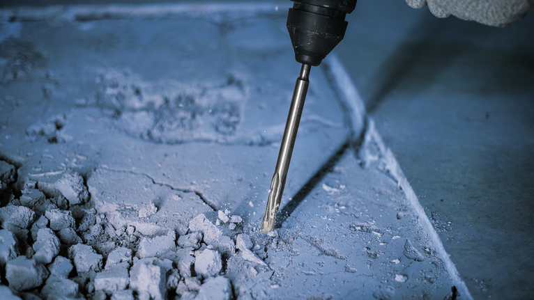 Seseorang yang mengenakan perlengkapan keselamatan menggunakan palu putar untuk memecahkan beton.