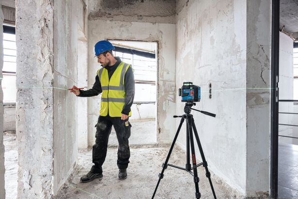 BT 150 Seseorang yang mengenakan peralatan keselamatan menandai dinding menggunakan alat perata laser pada tripod bangunan.