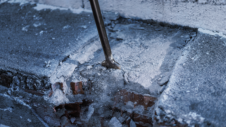 Pahat menerobos permukaan beton yang dipenuhi debu dan serpihan.