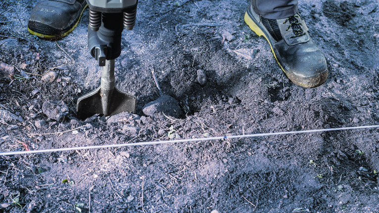 Pekerja yang mengenakan peralatan keselamatan menggunakan palu pembongkaran untuk memecah tanah.