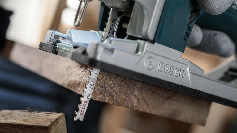 Orang yang mengenakan peralatan keselamatan menggunakan gergaji ukir untuk memotong papan kayu.