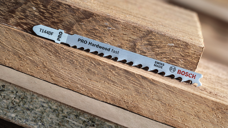 Mata gergaji ukir tergeletak di atas tumpukan potongan kayu keras.