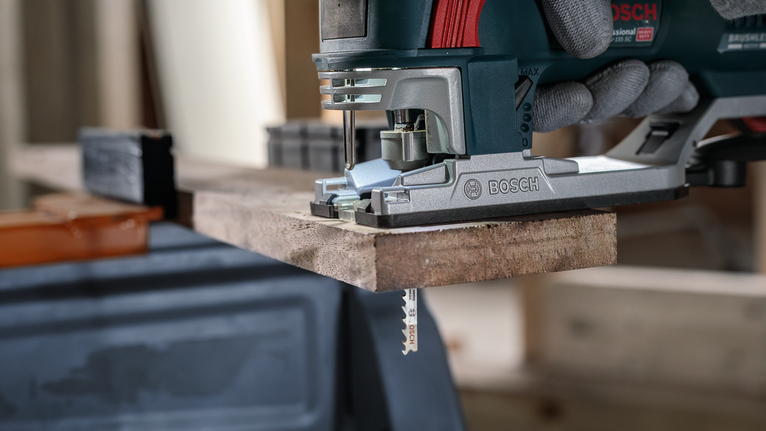 Orang yang mengenakan peralatan keselamatan menggunakan gergaji ukir untuk memotong papan kayu.