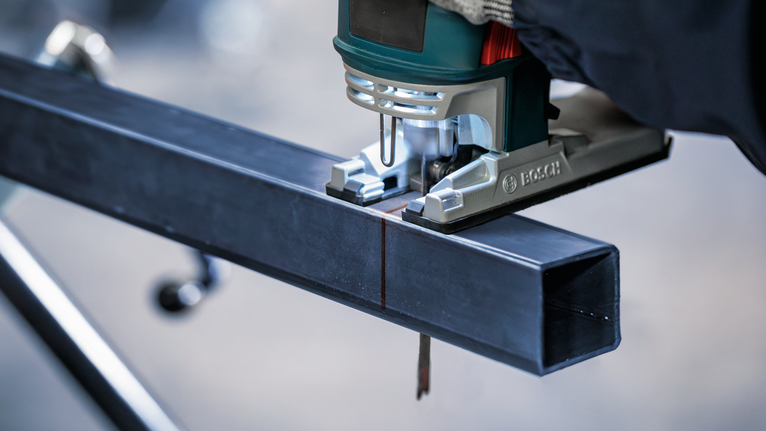 Orang yang mengenakan perlengkapan keselamatan menggunakan gergaji ukir untuk memotong balok logam.